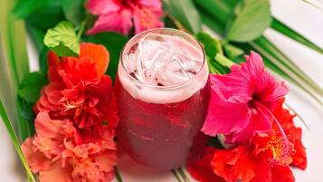 Un bicchiere di bevanda rossa con ghiaccio, circondato da fiori colorati.