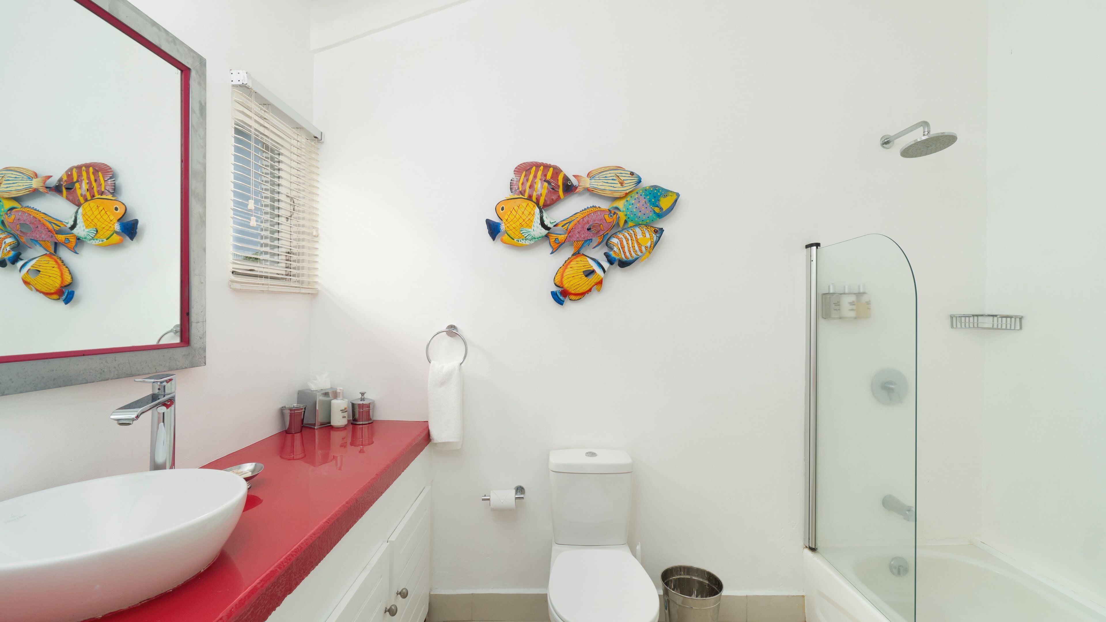 Une salle de bain avec un plan de toilette rouge, un lavabo blanc et une cabine de douche en verre.