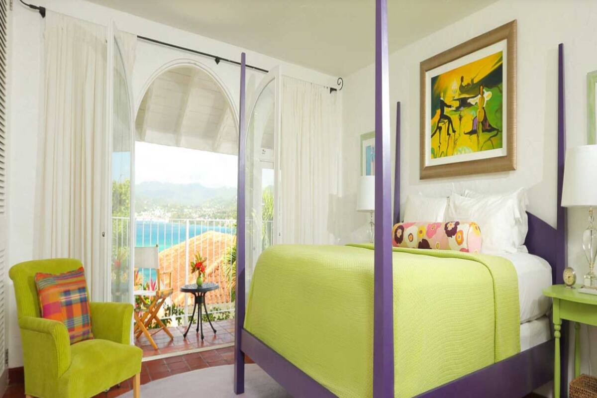 A bedroom with a bed, a chair, a table, and a painting on the wall.