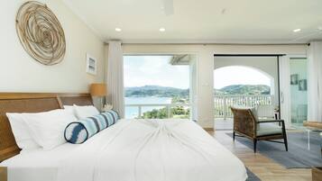 Ein Hotelzimmer mit einem großen Bett, Meerblick und einem Balkon mit einem Korbstuhl.