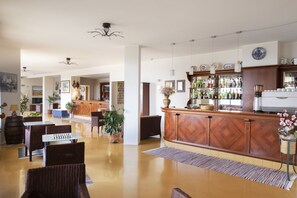 Un hall d’entrée spacieux avec un comptoir de réception en bois, un coin salon et un bar proposant un large choix de boissons.