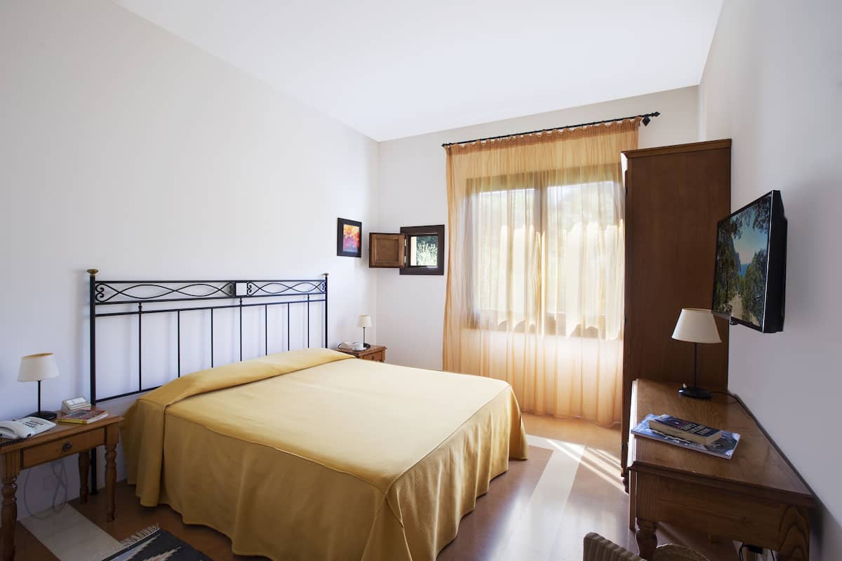 A hotel room with a bed, bedside table, lamp, and a large window with curtains.