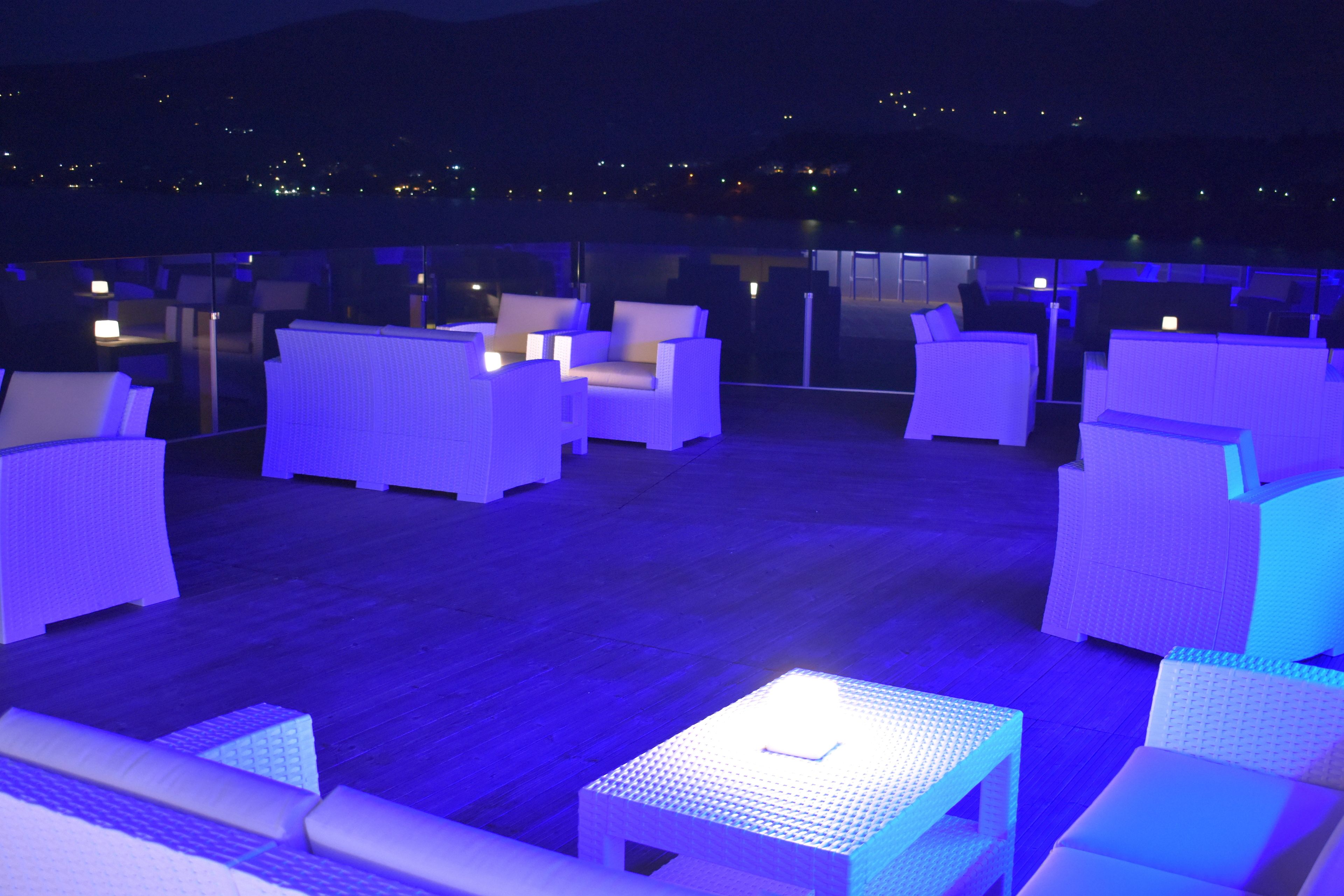 A rooftop lounge area with white wicker furniture and a small table with a light.
