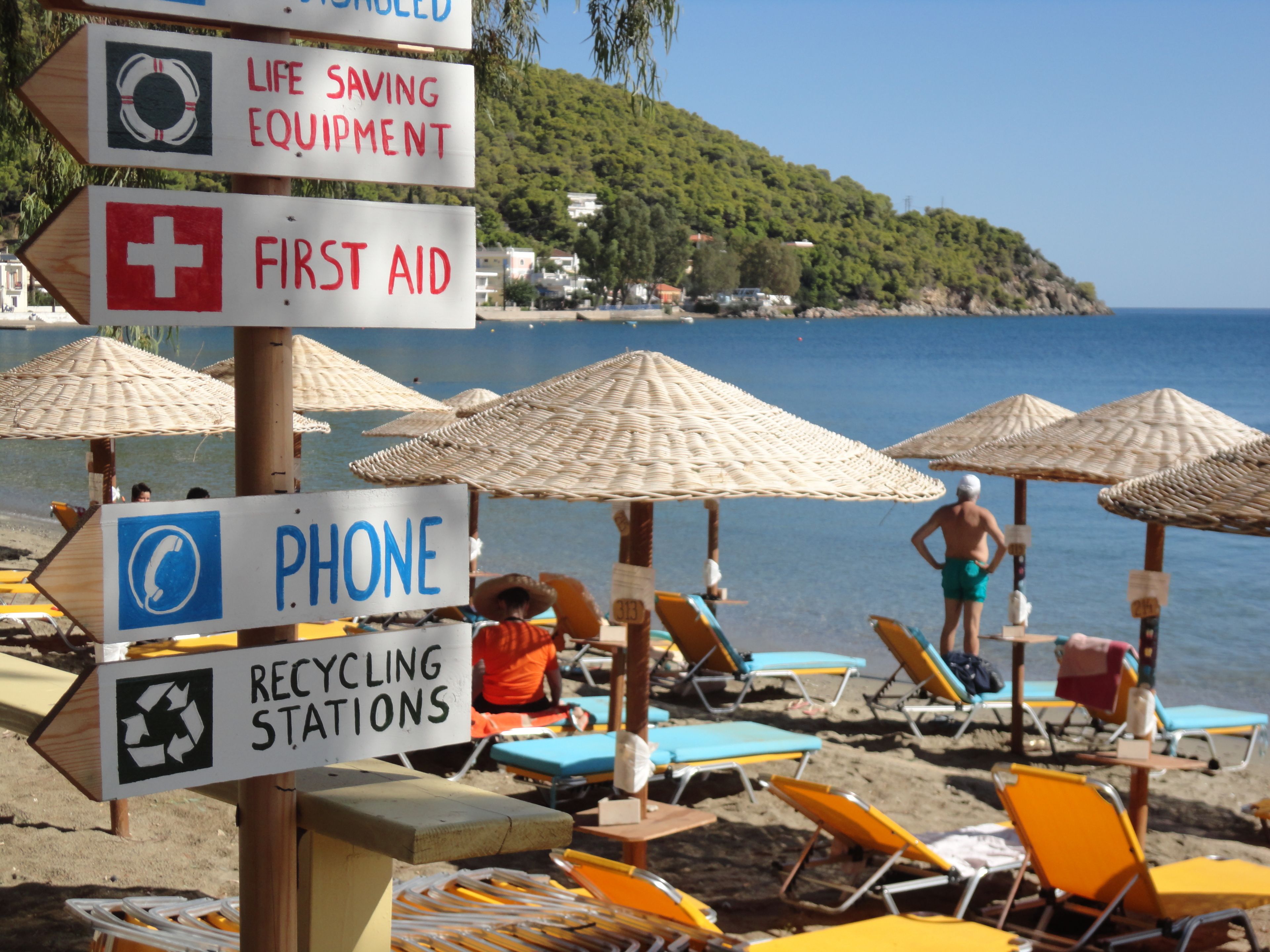 A beach with signs for life-saving equipment, first aid, phone, and recycling stations.