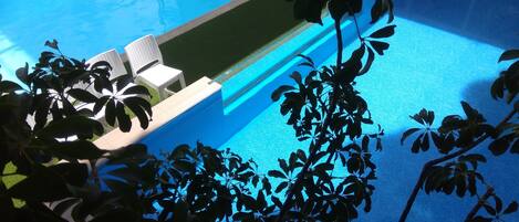 A swimming pool with a clear blue water surface, surrounded by a well-maintained lawn and white lounge chairs.
