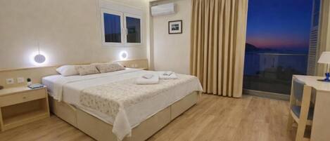 A hotel room with a bed, bedside tables, a window, an air conditioner, and a view of the sky.