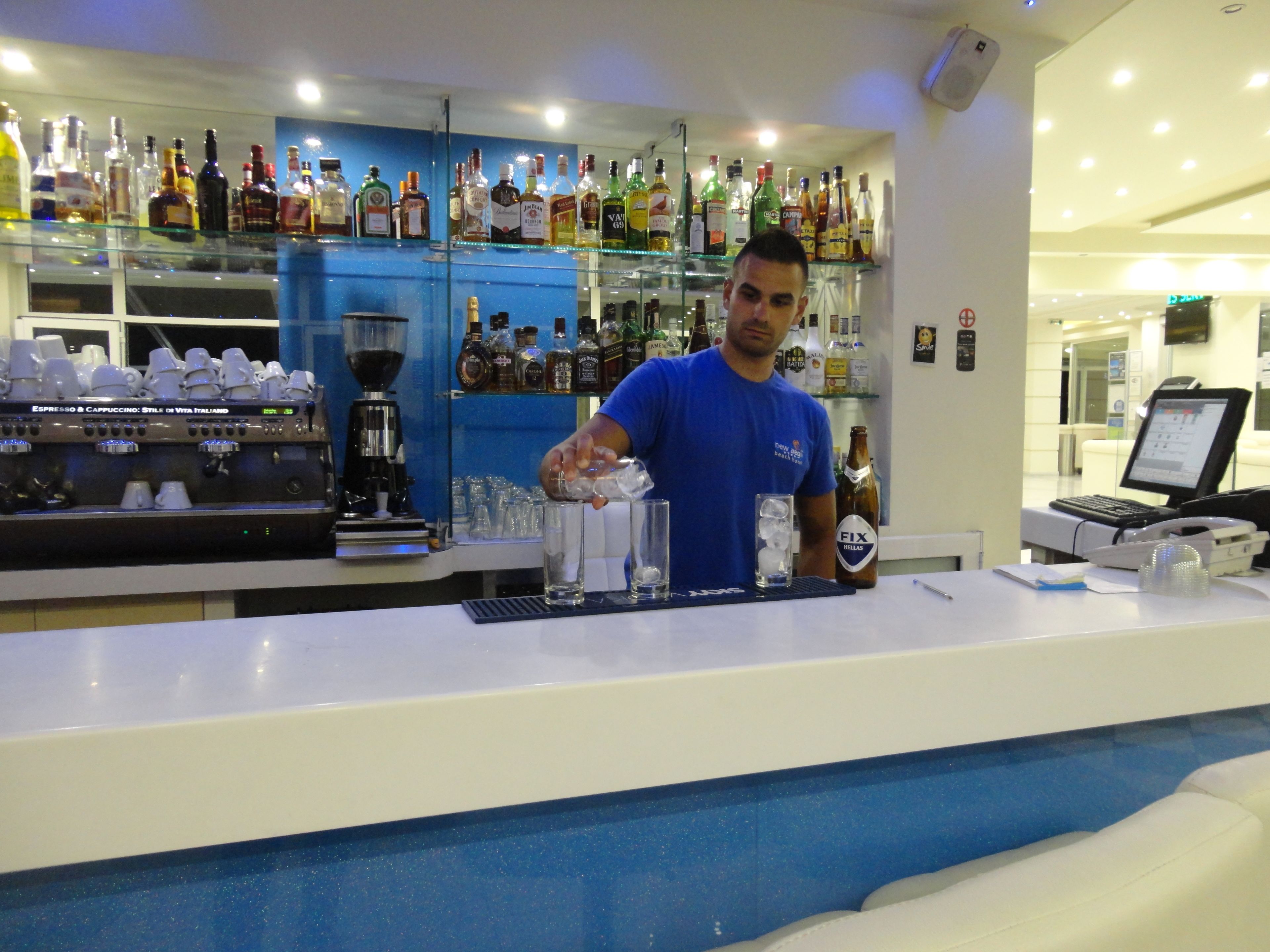 Zona de bar con un barman preparando bebidas, una máquina de café y una variedad de botellas de licor.