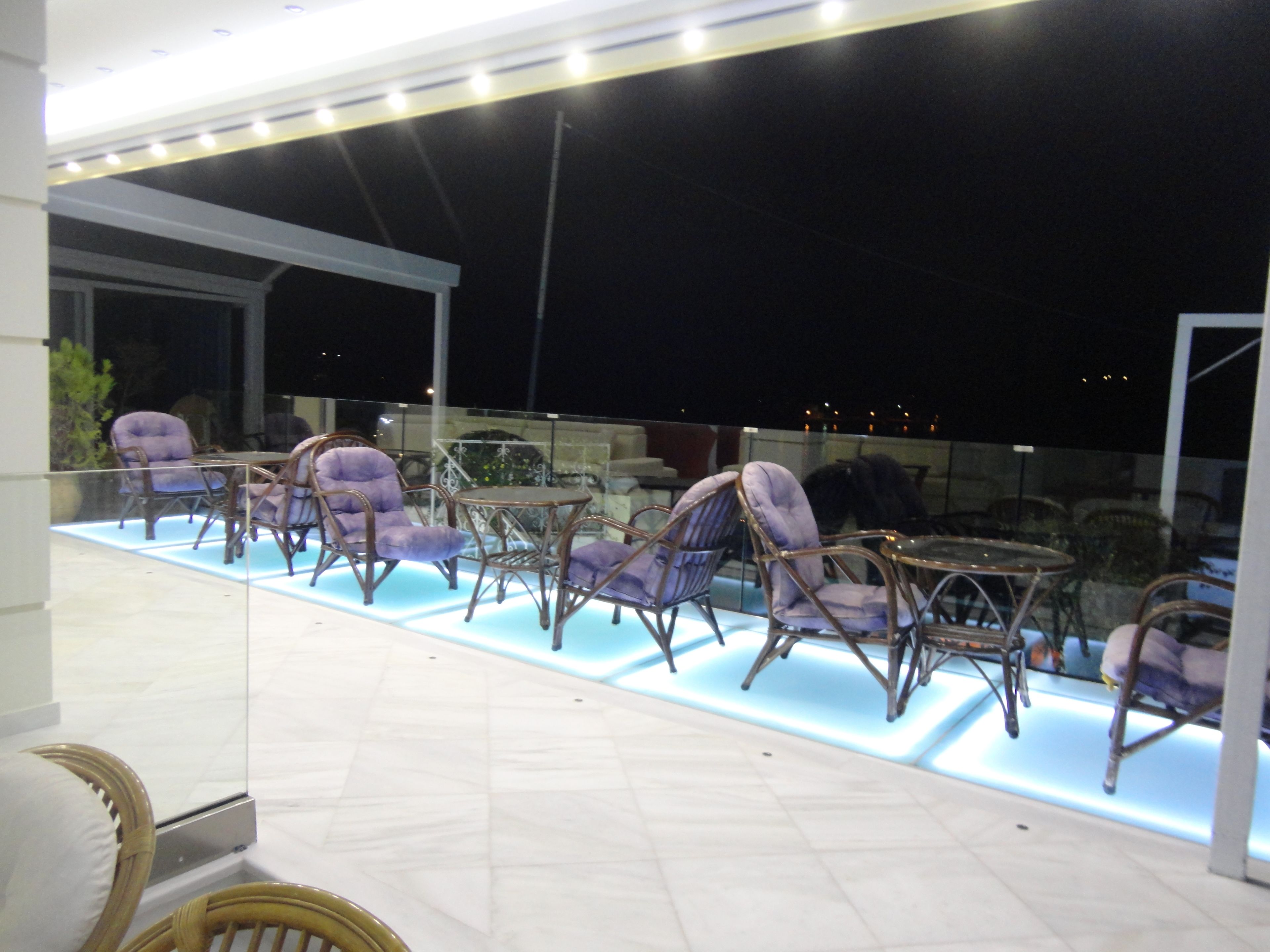 Een terras met rieten stoelen en een glazen tafel, verlicht met inbouwverlichting.