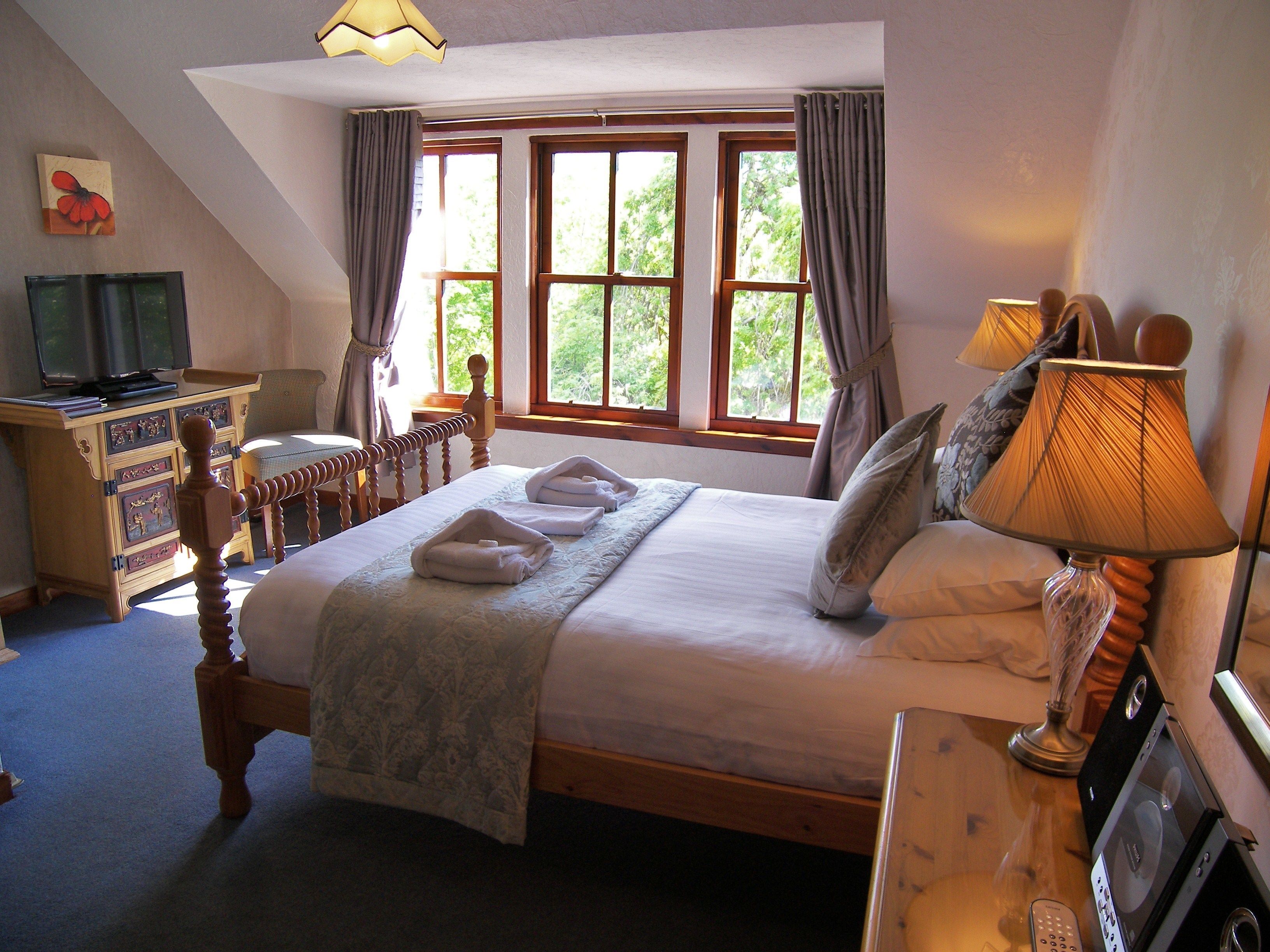 A bedroom with a bed, a desk, a television, and a window with curtains.