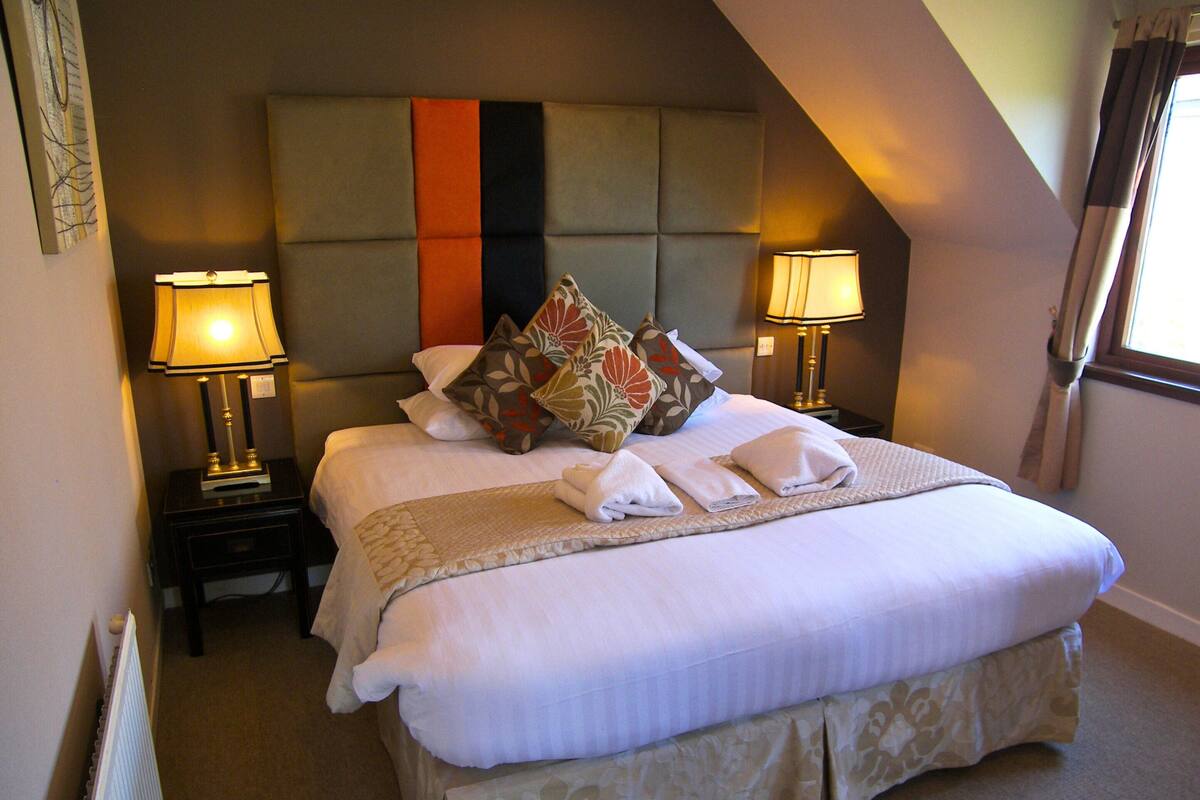 A neatly made bed with pillows and a blanket, two bedside lamps, and a headboard with a striped design.