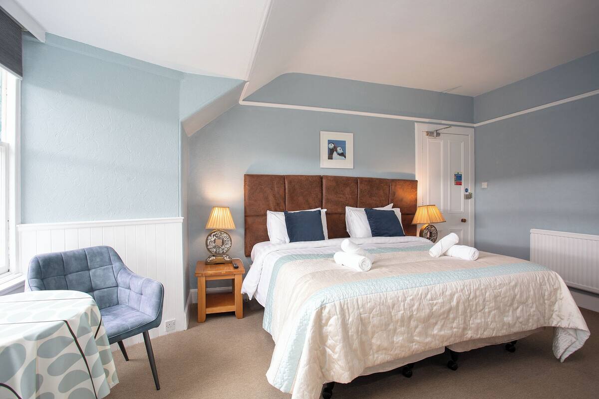 A bedroom with a bed, a chair, a nightstand, and a table.