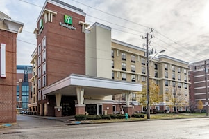 Un hotel Holiday Inn con fachada de ladrillo, entrada cubierta y estacionamiento.