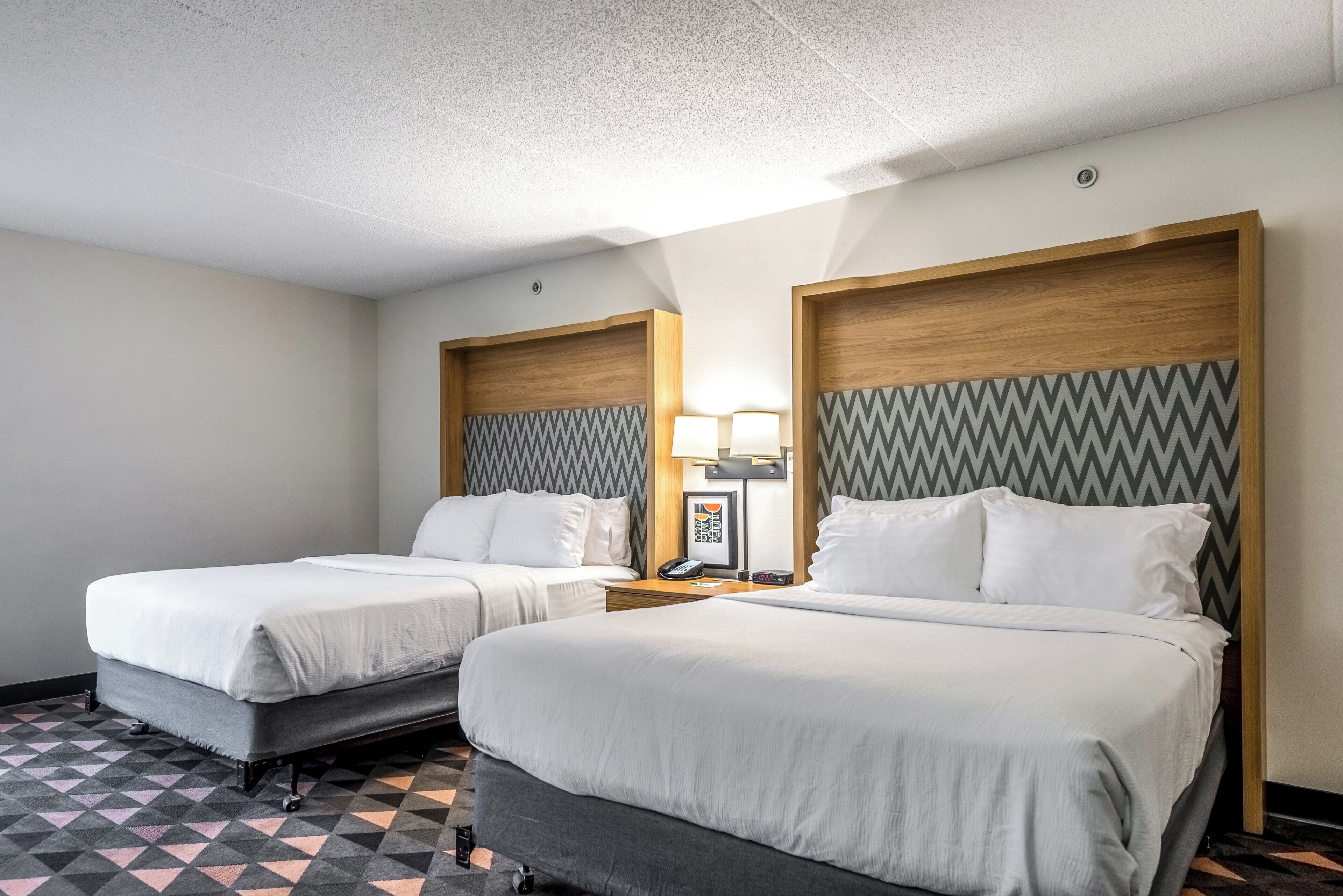 Ein Hotelzimmer mit zwei Betten, einem gemusterten Boden und einem Holz-Kopfteil mit Zickzackmuster.