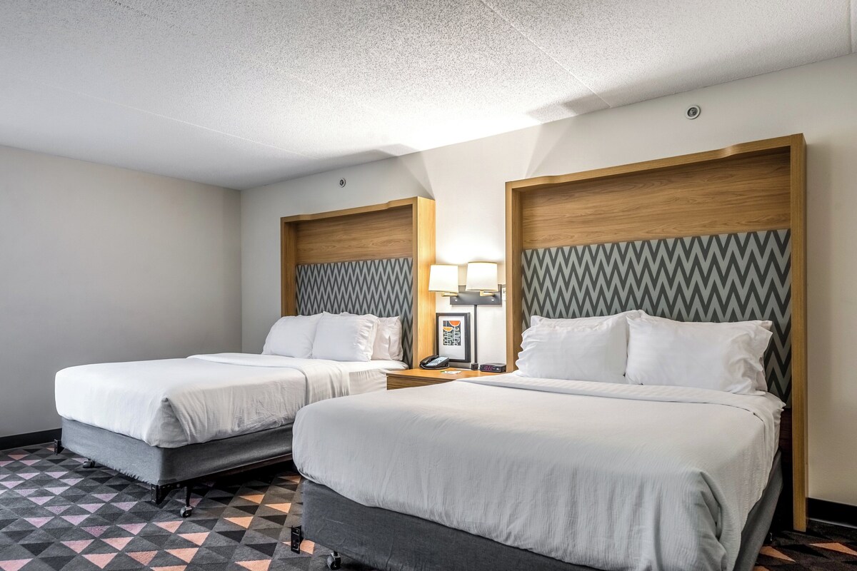 A hotel room with two beds, a patterned floor, and a wooden headboard with a chevron design.