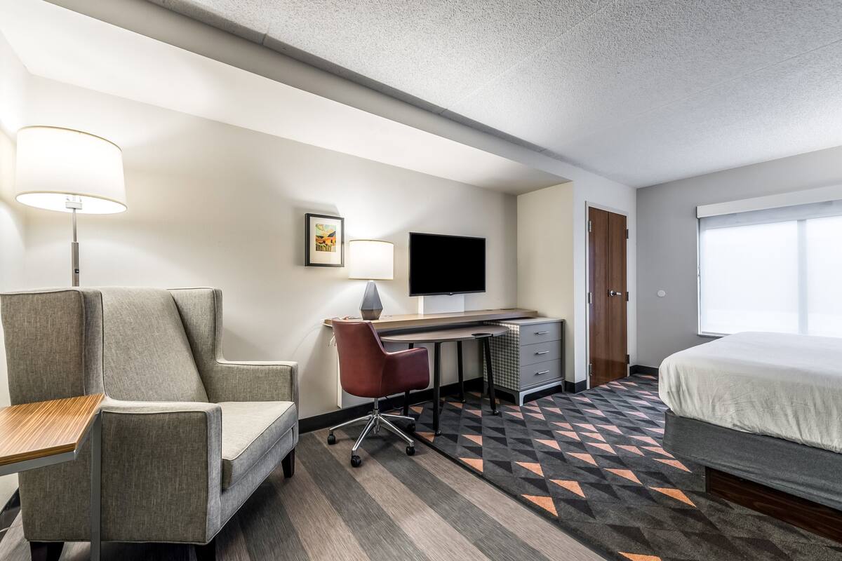 A hotel room with a bed, a desk, a chair, a TV, and a picture on the wall.