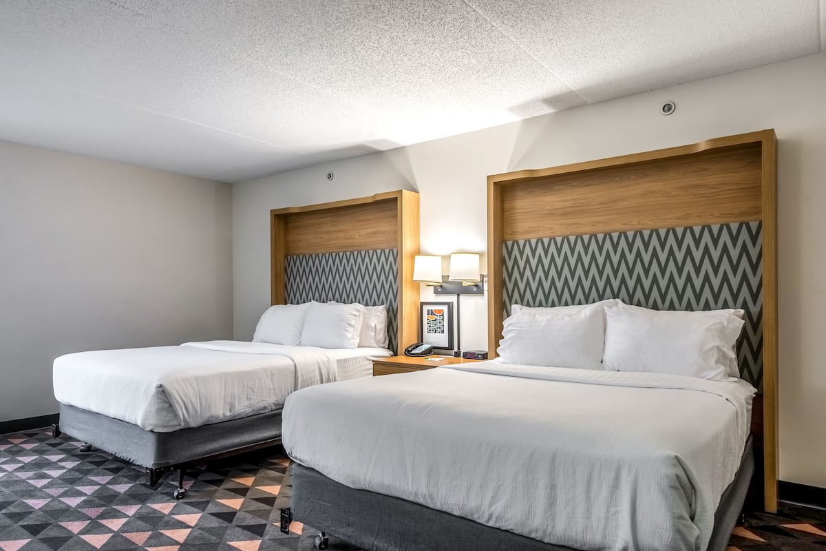 A hotel room with two beds, a patterned floor, and a wooden headboard with a zigzag design.
