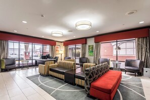 A hotel lobby with a seating area, a reception desk, and large windows offering a view of the outside.