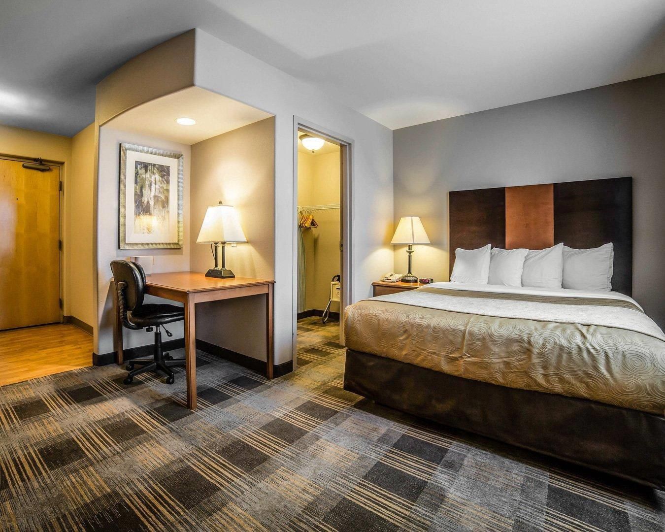 A hotel room with a bed, desk, chair, two lamps, and a framed picture on the wall.