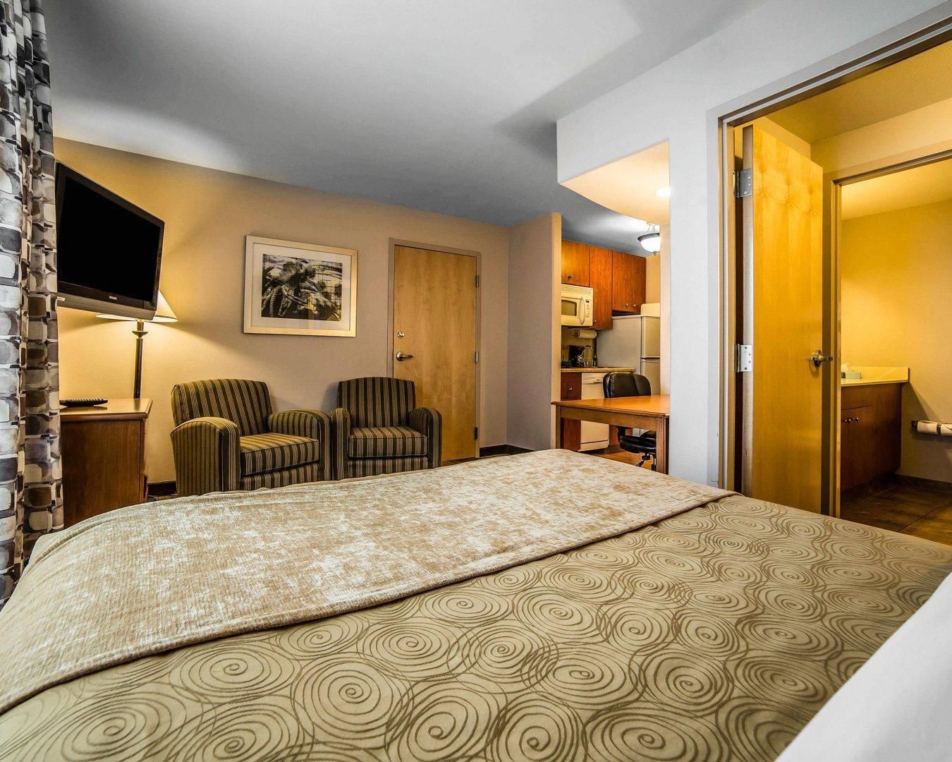Habitación de hotel con una cama, dos sillones a rayas, un televisor, un escritorio con microondas y una puerta de madera.