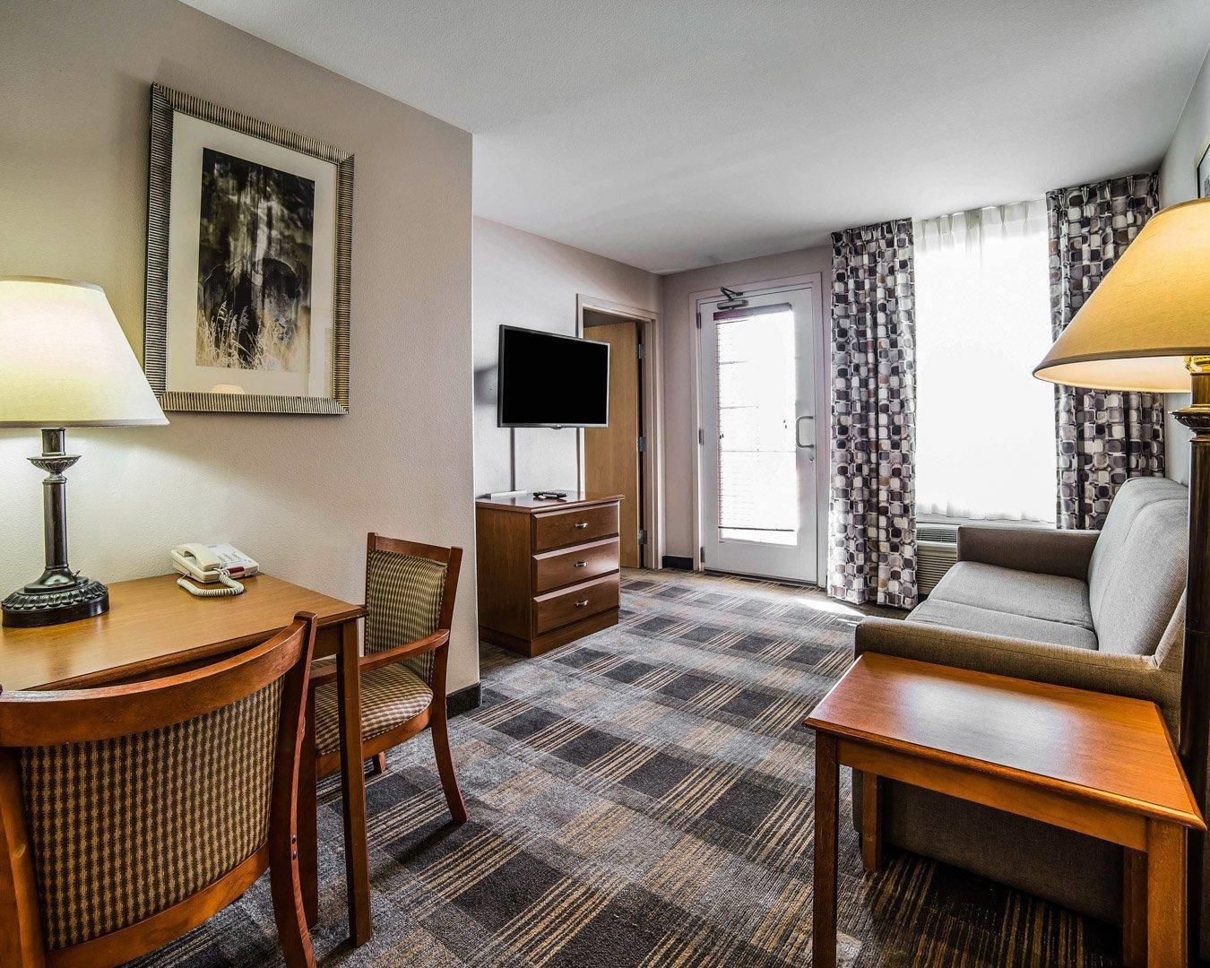A hotel room with a desk, chair, sofa, television, and a patterned carpet.