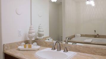 Ein Badezimmer mit Waschbecken, zwei Wasserhähnen, einem Spiegel, einer Leuchte und einer Badewanne.