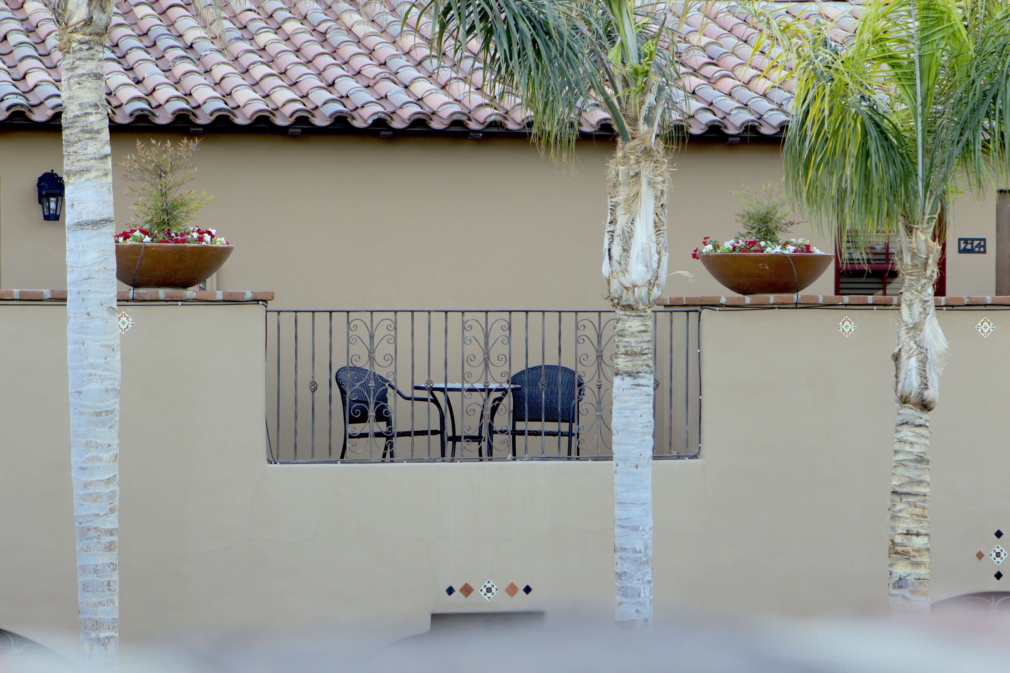Een balkon met twee stoelen en een tafel, een betegeld dak en twee grote bloempotten.