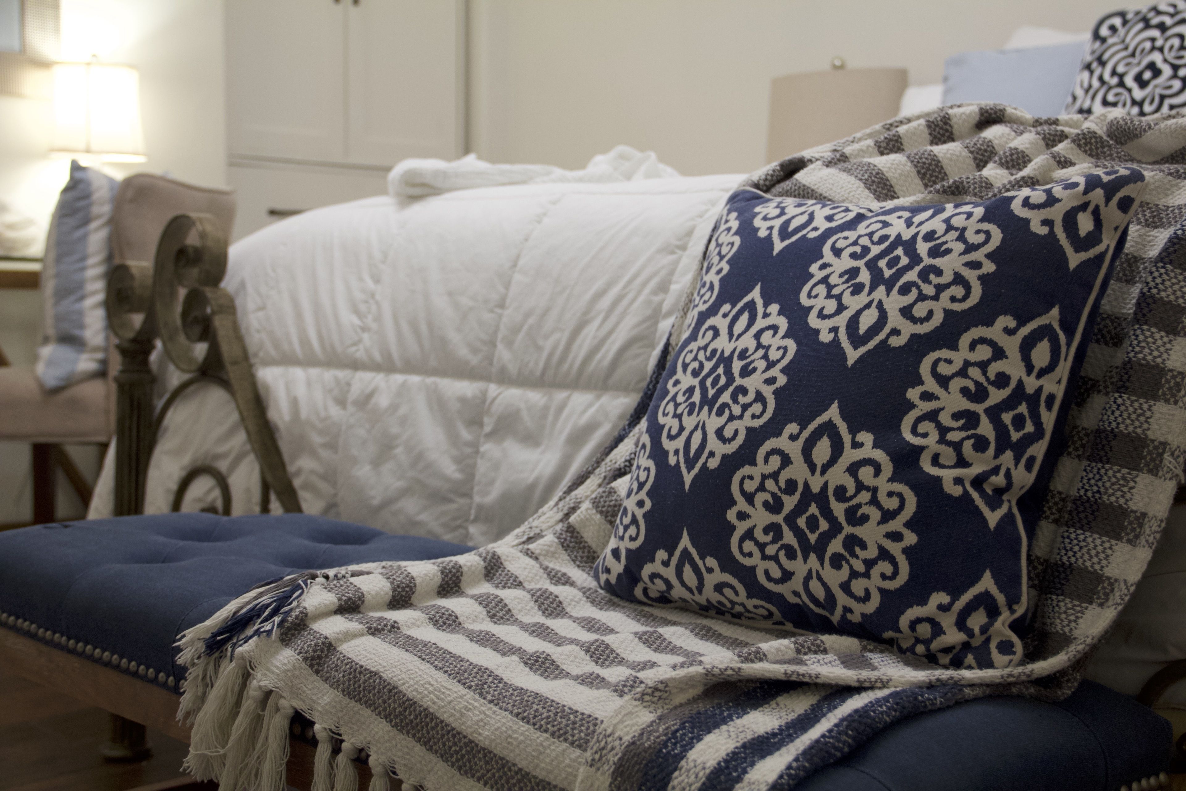 A bed with a white quilt and a blue and white patterned pillow.