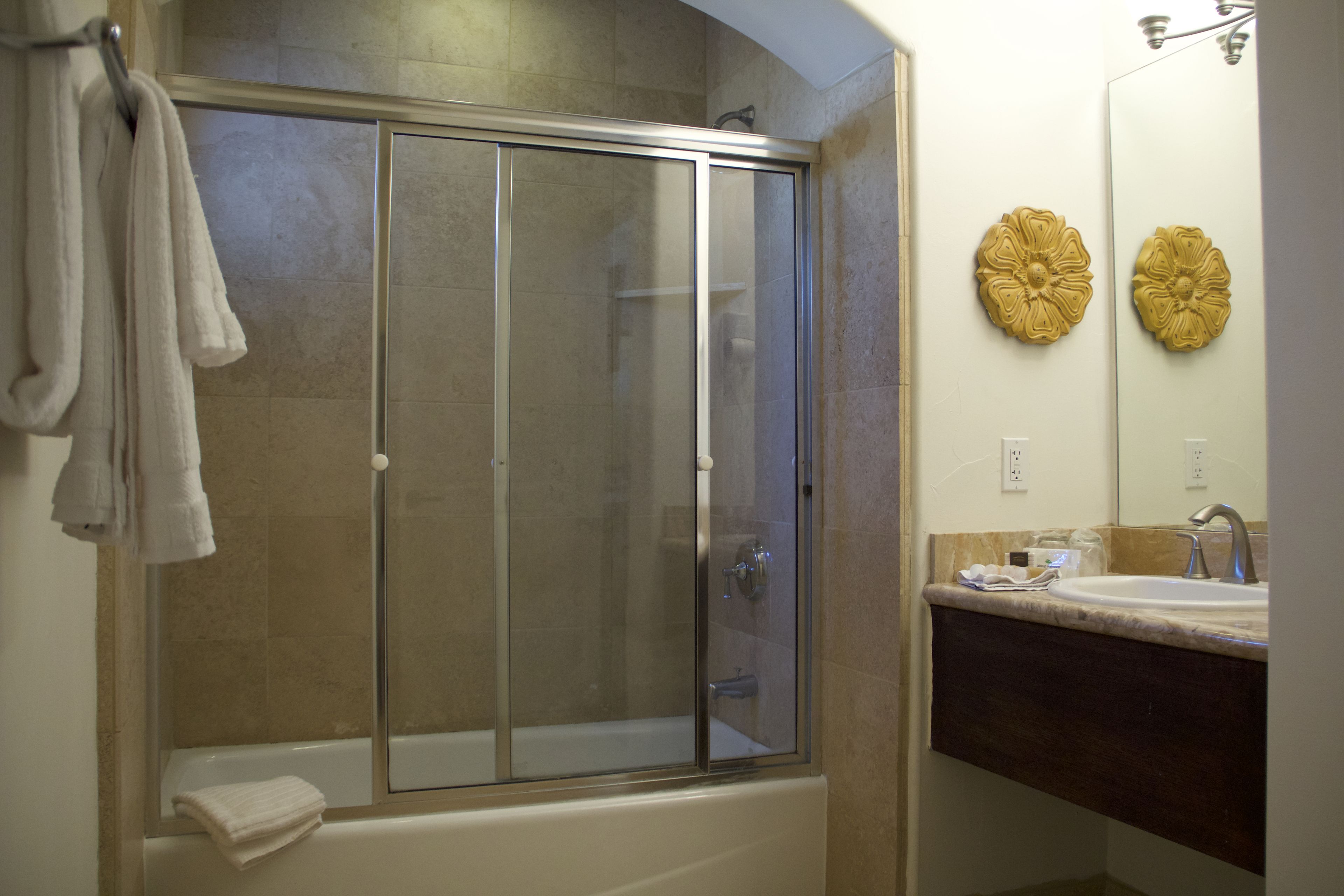 Un baño con ducha de vidrio, bañera, lavamanos y dos adornos florales en la pared.