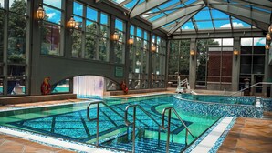 An indoor swimming pool with clear glass walls, metal railings, and a tiled floor.
