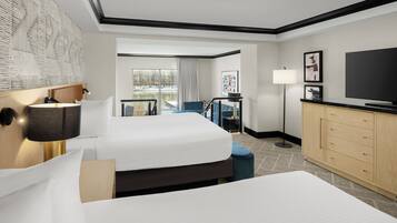A hotel room with two beds, a TV, a desk, and a view of a lake.