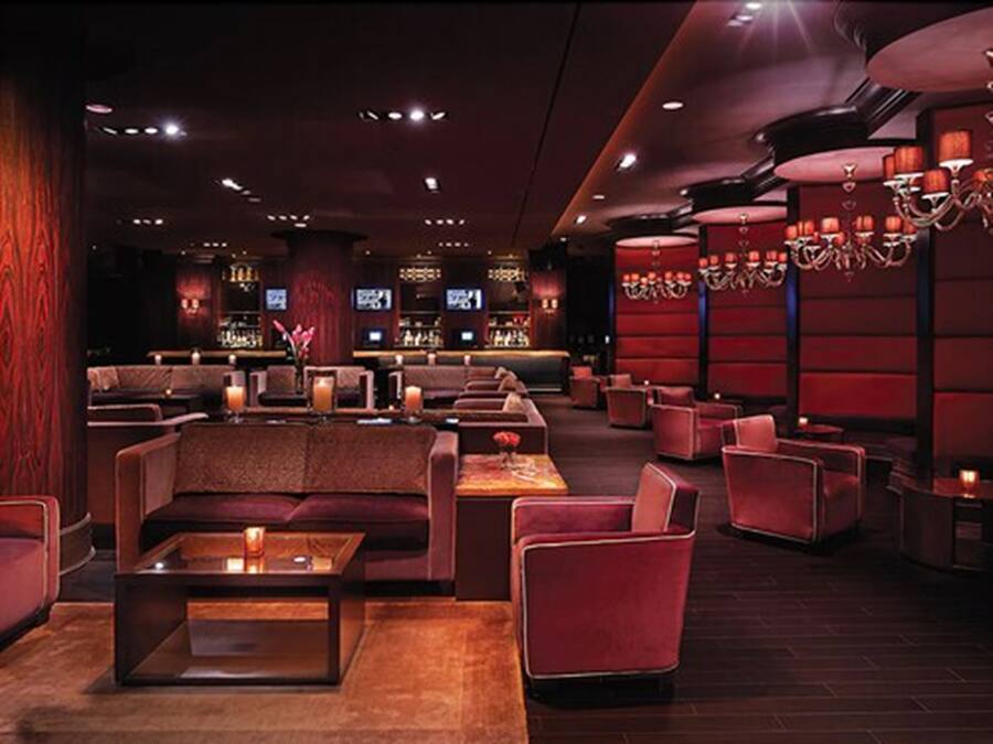 A dimly lit lounge area with plush seating, a bar in the background, and ambient lighting.