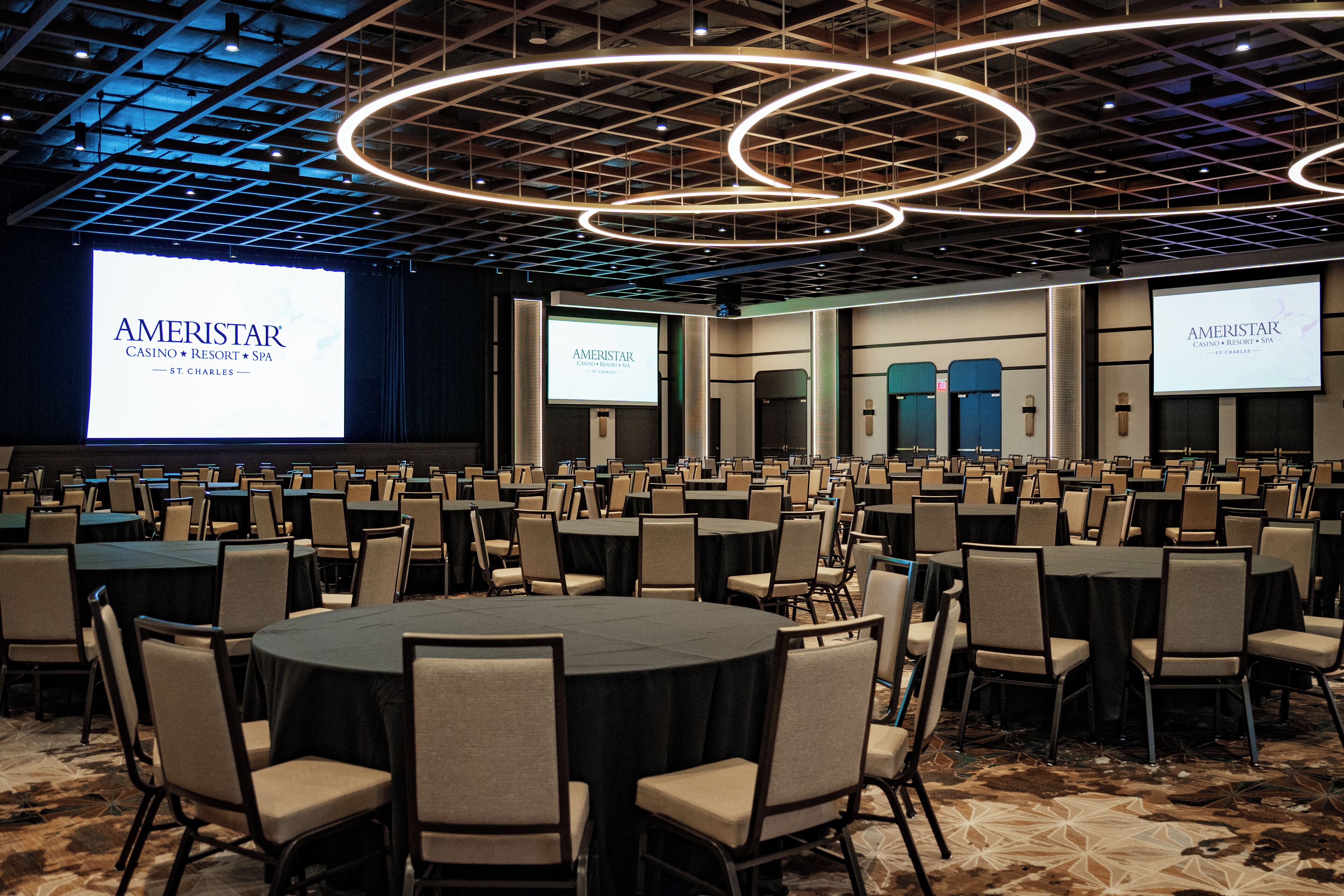 A conference room with multiple tables and chairs, a large screen displaying 'AMERISTAR,' and a modern ceiling design.