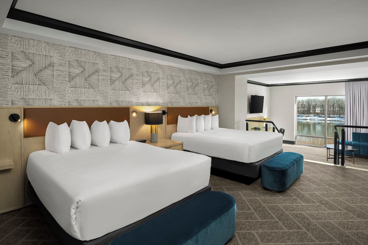 Habitación de hotel con dos camas, un ventanal con vistas, pared con diseño y un escritorio con lámpara.