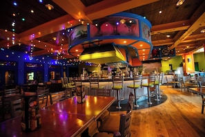 A restaurant with wooden tables and chairs, a bar area, and a curved ceiling with hanging lights.