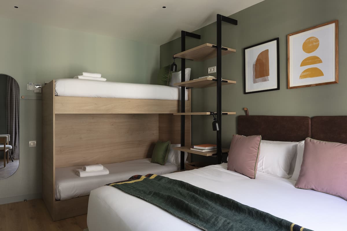 A bunk bed with a wooden headboard, a bedside table with a lamp, and a wall-mounted shelf.