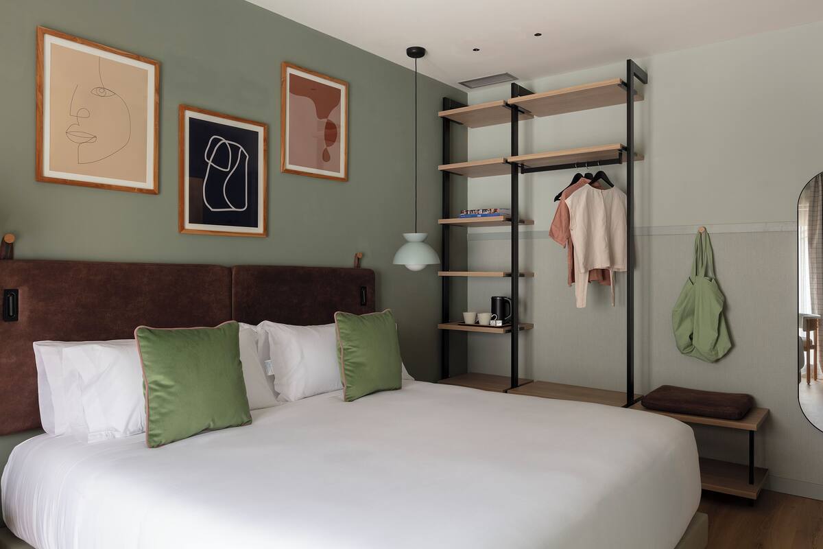 A neatly arranged bedroom with a large bed, a bedside table, a wardrobe, and wall art.