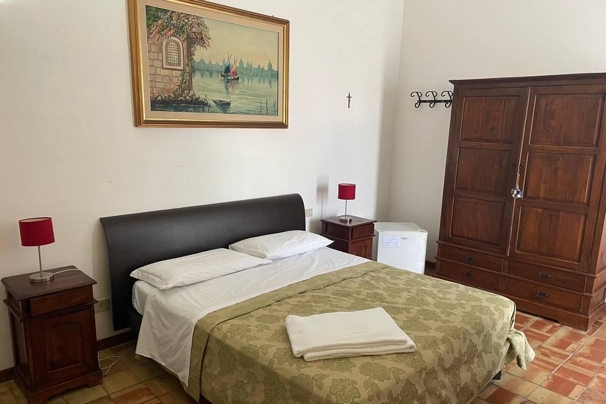 A bedroom with a bed, a nightstand, a lamp, a wardrobe, and a painting on the wall.