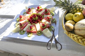 A fruit platter with various fruits and a basket of bananas and apples on a table.