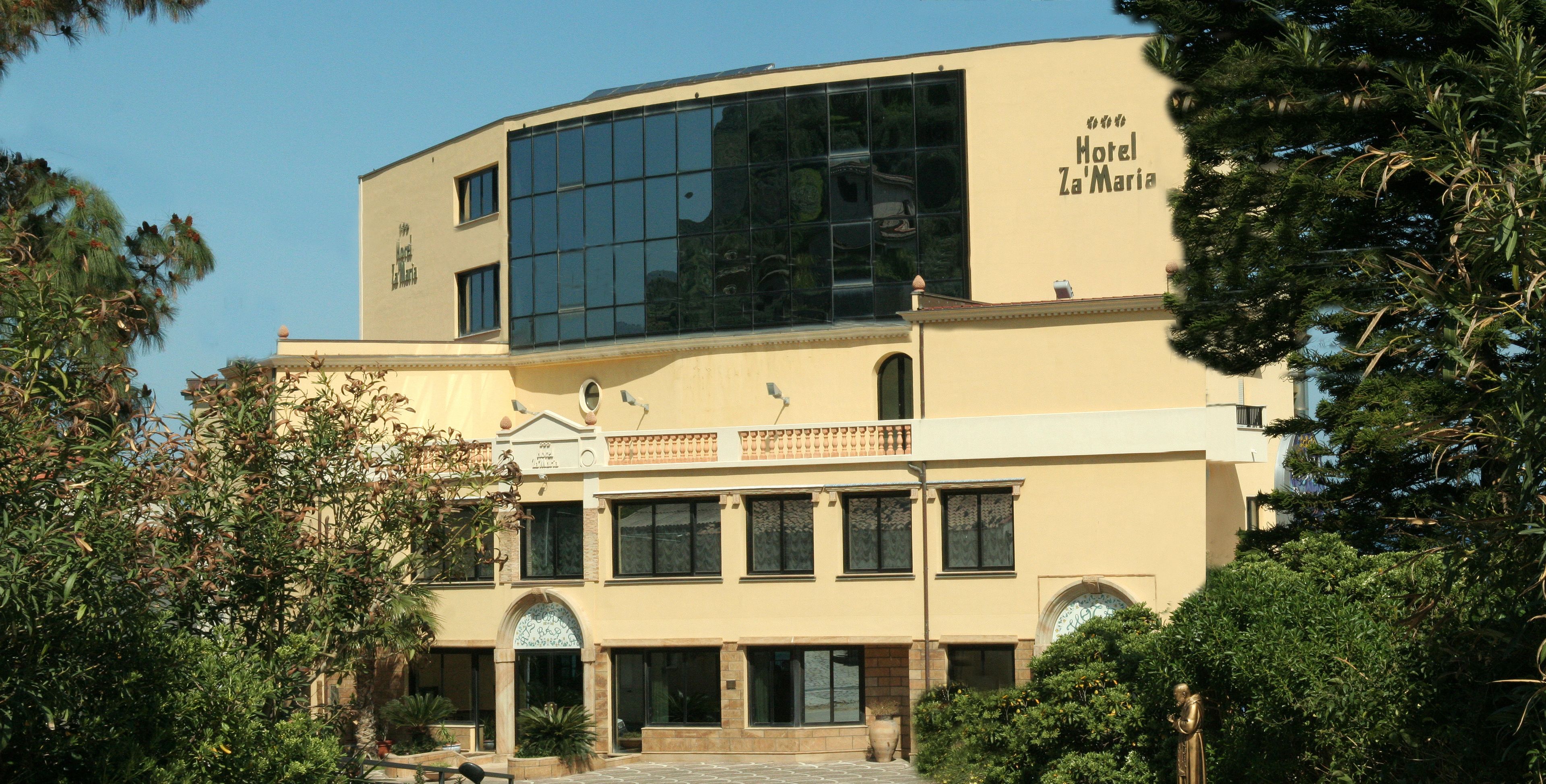 A two-story building with a large glass facade, a balcony, and a sign reading "Hotel Za'Maria".