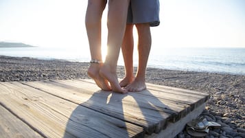A wooden platform on a pebbled beach with a pair of feet standing on it.