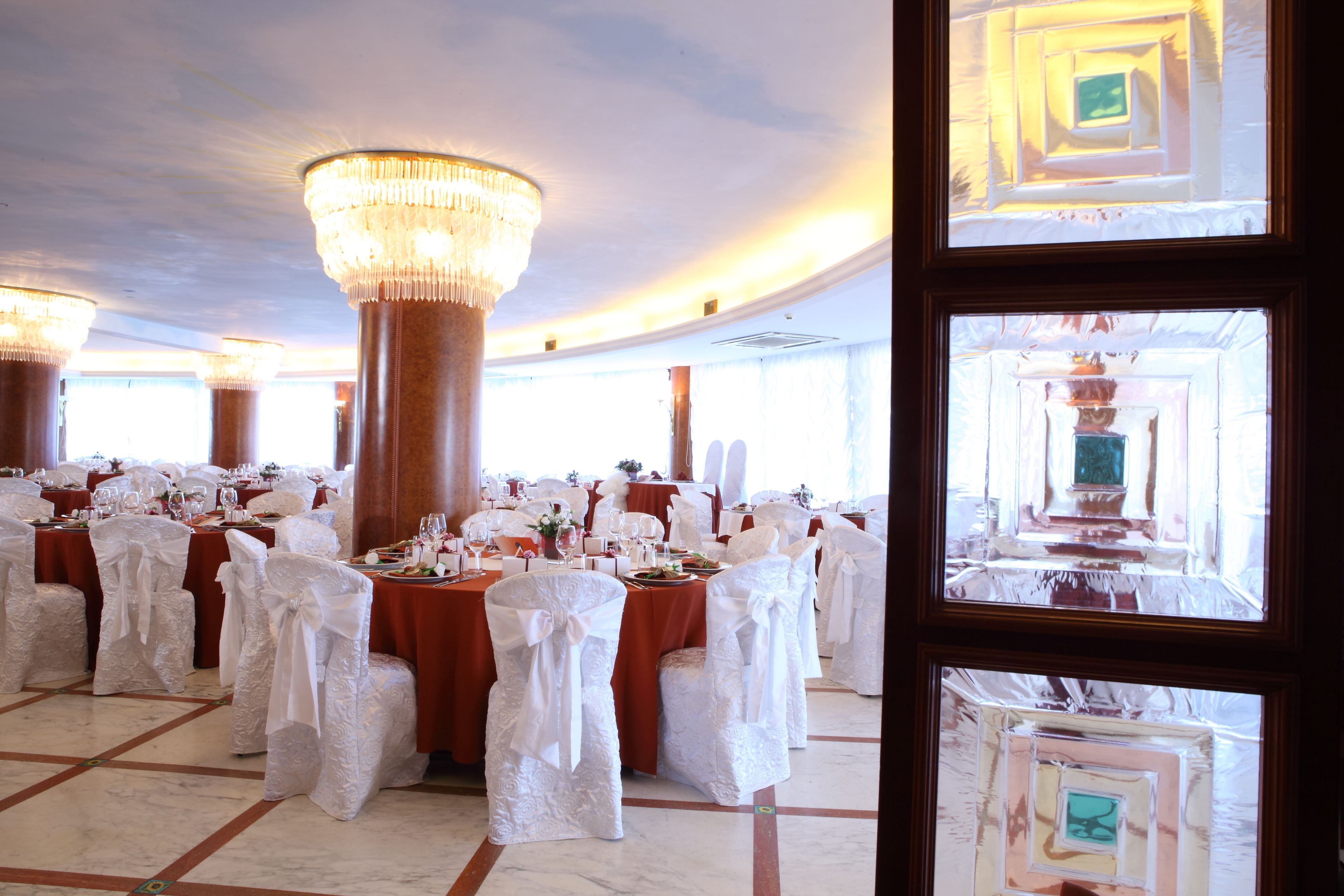 Un salón de banquetes con mesas redondas, sillas blancas y candelabros.