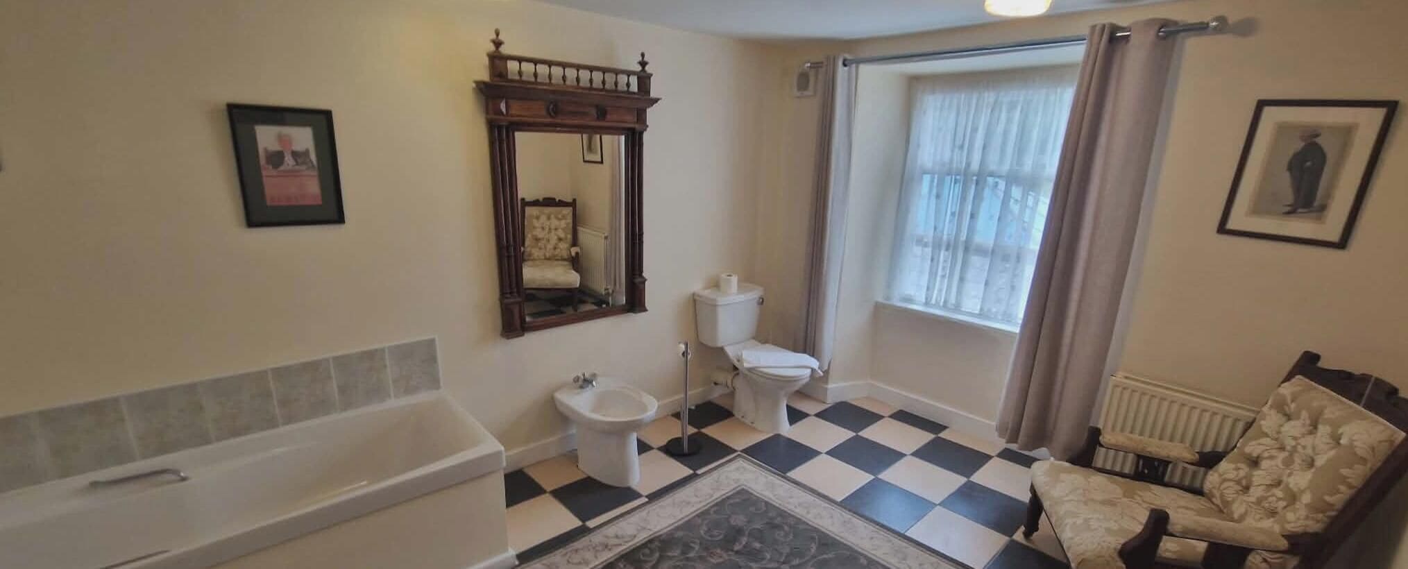 Uma casa de banho com banheira, sanita, bidé e uma janela grande com cortinas.