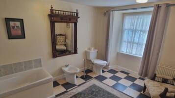 Uma casa de banho com banheira, sanita, bidé e uma janela grande com cortinas.