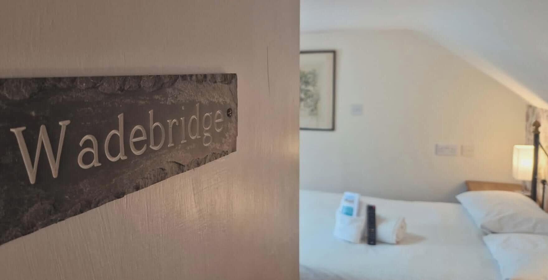 A sign with the name 'Wadebridge' and a bedroom with a bed, pillows, a remote control, and a lamp.