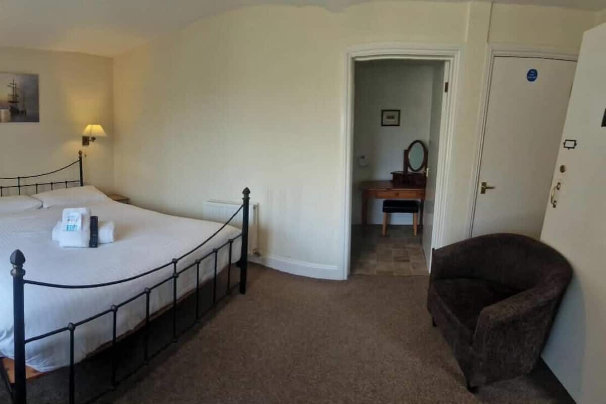 A bedroom with a single bed, bedside lamps, a window with curtains, a chair, and a door leading to another room.