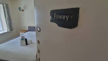 A hotel room with a bed, a nightstand, a lamp, and a sign that reads 'Fowey.'