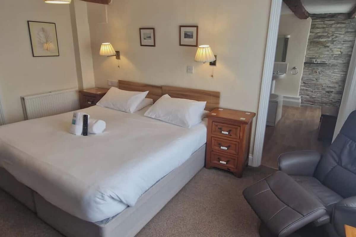 A hotel room with a bed, bedside lamps, a chair, and a stone wall.