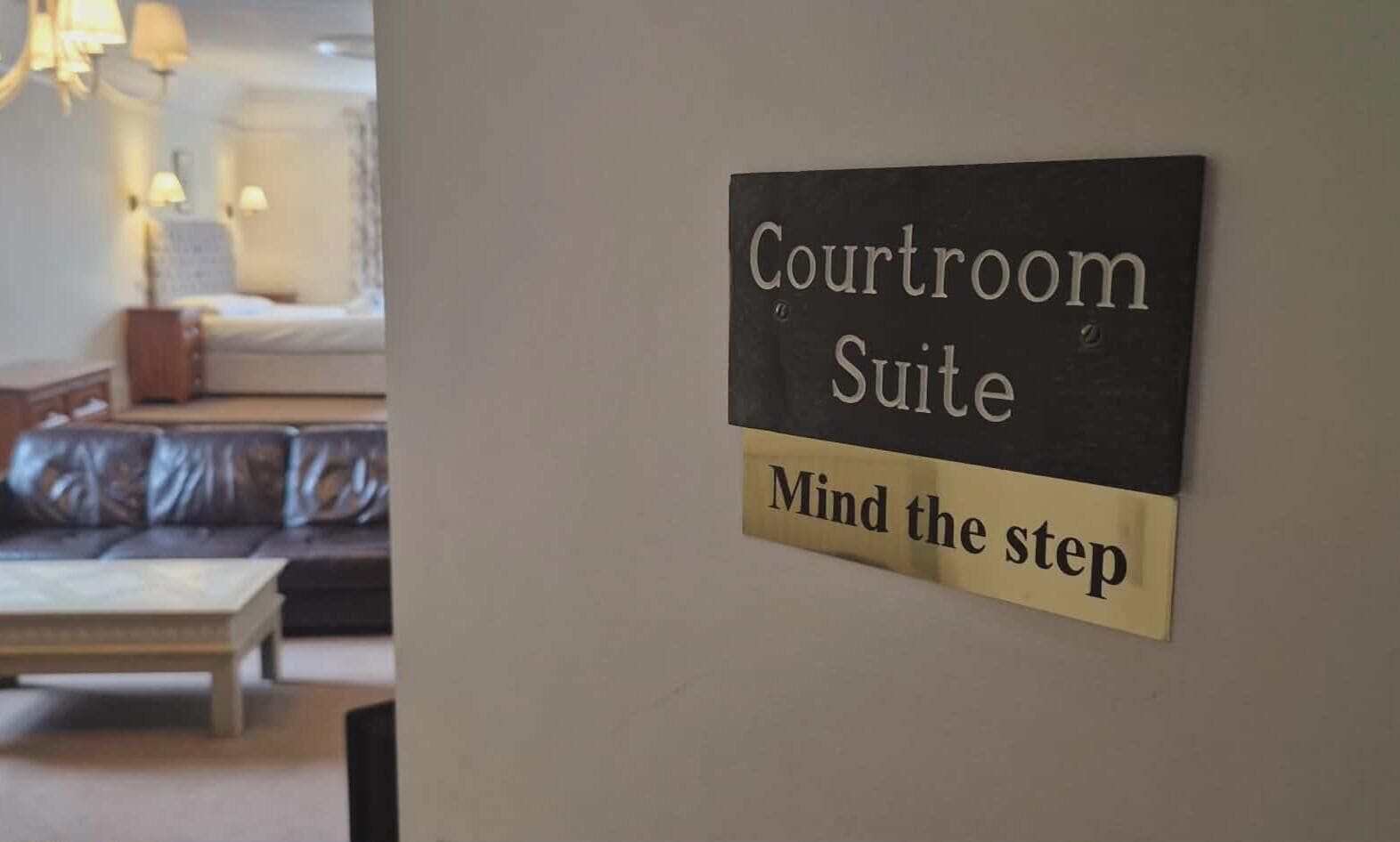 A sign indicating a 'Courtroom Suite' with a humorous note 'Mind the step' on a wall.