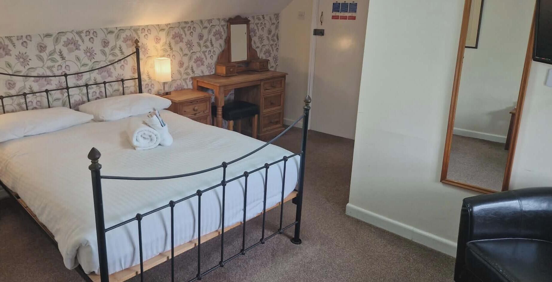 A bedroom with a bed, a nightstand, a dresser, a mirror, and a chair.