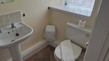 A small bathroom with a white sink, toilet, and a window above the toilet.